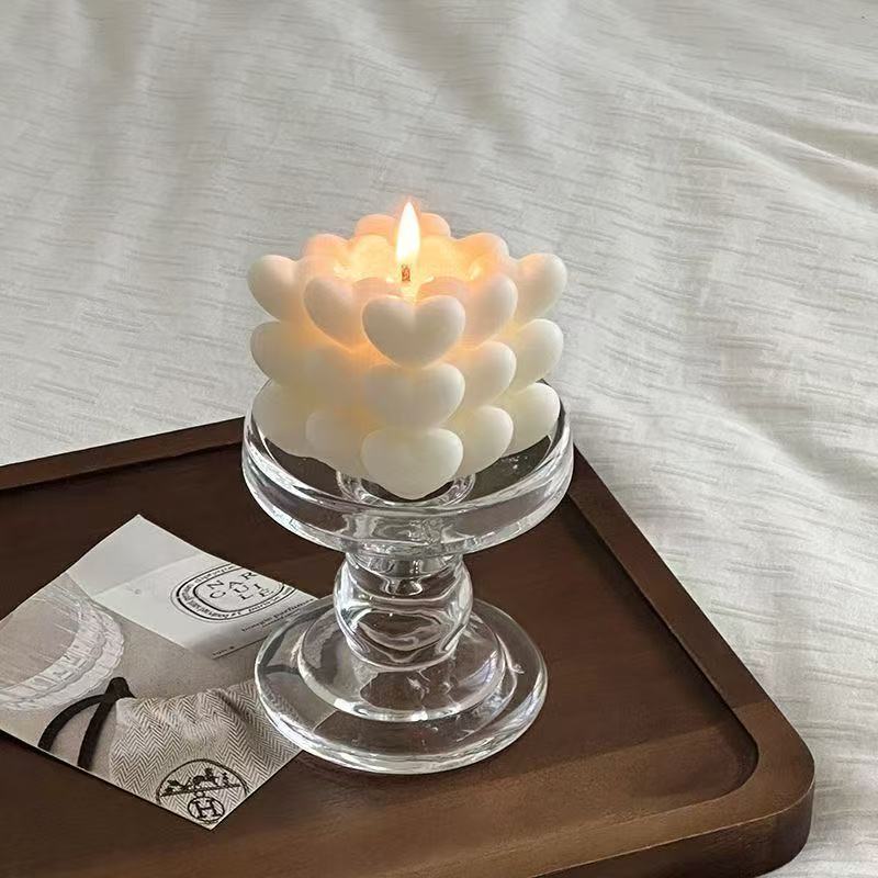 Candle with heart-shaped design in a glass holder on a wooden tray.